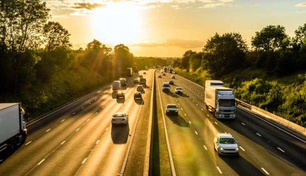 A busy UK motorway at sunset with cars and lorries traveling in both directions