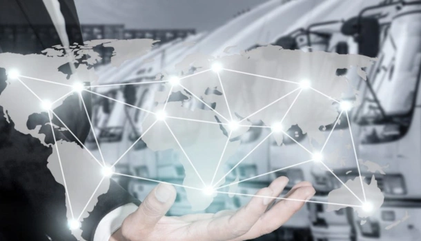 Businessperson holding a digital world map with glowing connection points in front of a row of white logistics trucks