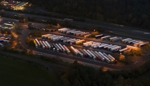 Aerial view of a large, well-lit UK truck stop at night with rows of parked lorries and surrounding service station buildings near a motorway