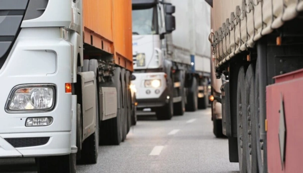 A row of large freight trucks sits in traffic on a highway