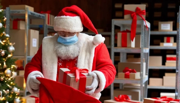 Santa Claus wearing a face mask and sorting wrapped presents in a warehouse filled with packages