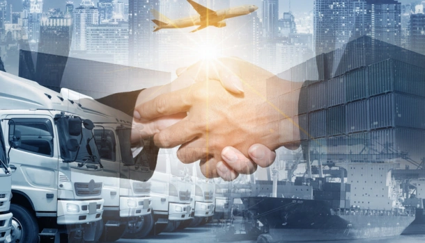 Two businesspeople shaking hands overlaid on a background of trucks, a cargo ship, containers, and an airplane
