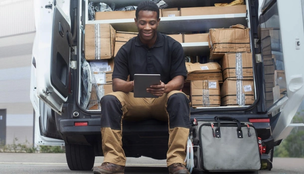 A delivery worker sits on the edge of an open van filled with packages