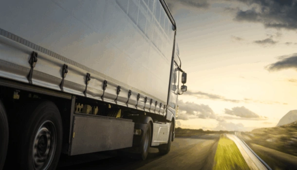 Side view of a large cargo truck driving on an open highway at sunset