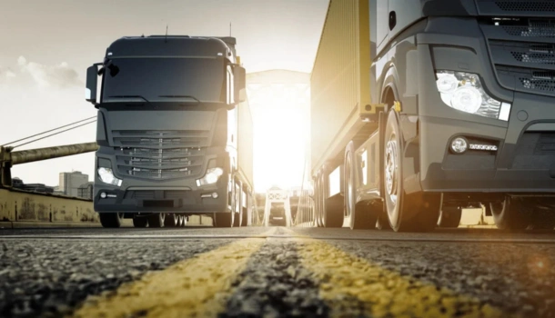Low-angle view of large black freight trucks driving across a bridge at sunrise