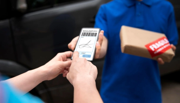 Delivery driver holding a package while a customer signs on a smartphone screen
