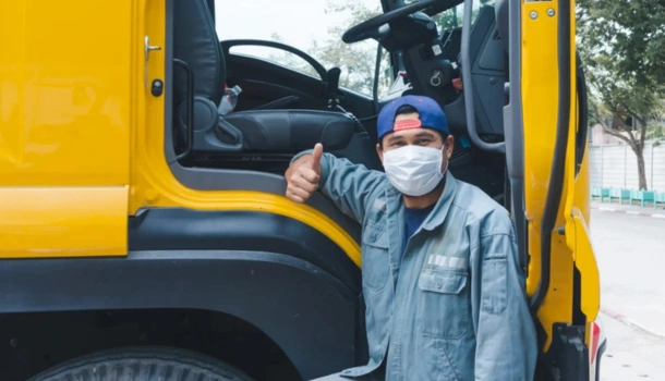 A delivery driver wearing a face mask and blue work uniform gives a thumbs-up
