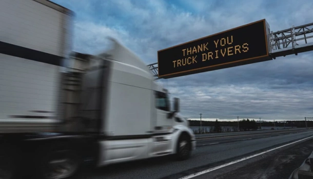 A white truck drives under a highway sign that reads "THANK YOU TRUCK DRIVERS"