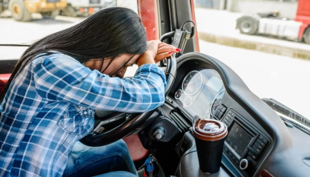 A woman truck driver resting her head on the steering wheel, showing signs of exhaustion or stress