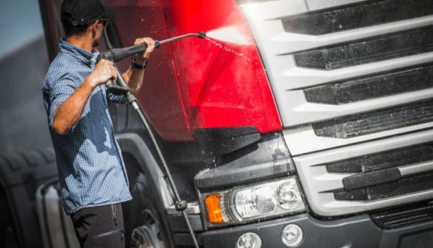 Man using a high-pressure hose to clean the front of a red HGV truck