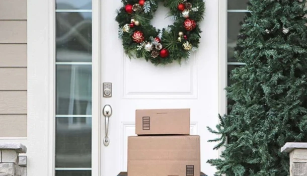 A stack of cardboard delivery boxes sits on a doorstep decorated with a festive Christmas wreath