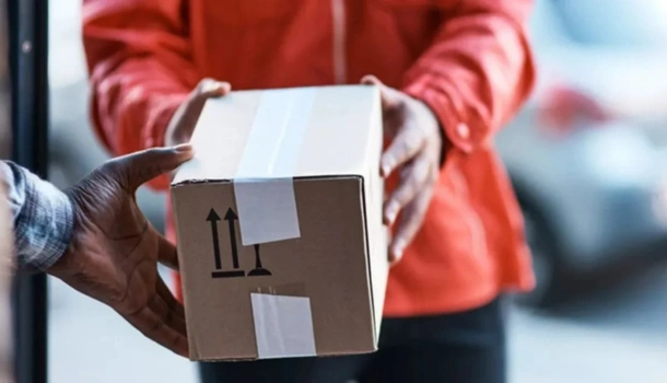 Close-up of a person in a red jacket handing over a cardboard package during a last-mile delivery