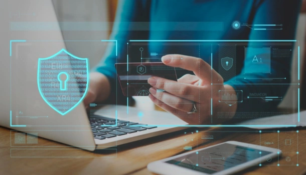 Person using a laptop and smartphone with digital cybersecurity interface graphics overlaid