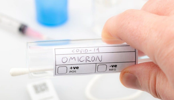 A hand holds a COVID-19 test tube labeled "Omicron" with positive and negative checkboxes