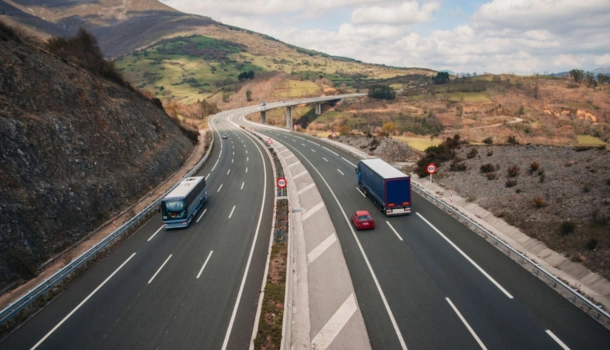 A wide open highway with a truck, car, and bus driving through a mountainous rural landscape