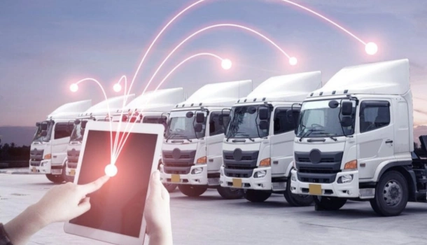 Person using a tablet to manage a fleet of white cargo trucks, with digital network lines connecting to each vehicle