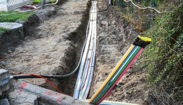 A trench with exposed multi-colored fiber optic cables being laid underground