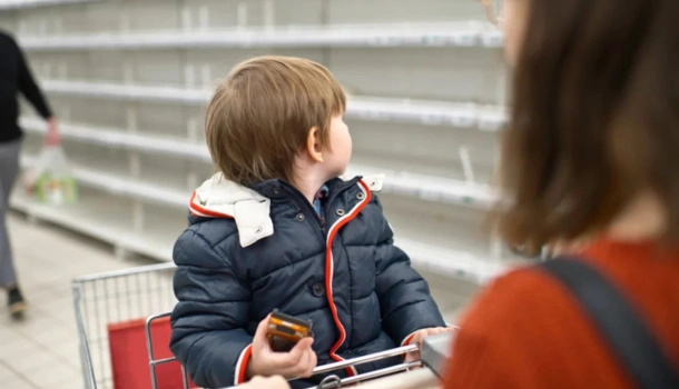 Young child sitting in a shopping cart looking at empty supermarket shelves