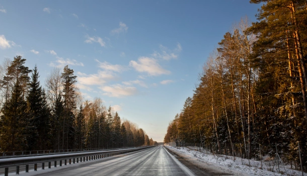 Empty icy highway surrounded by snow-covered trees on a clear winter day